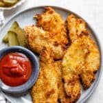 Plate of pickle brined chicken tenders with ketchup and pickles on the side