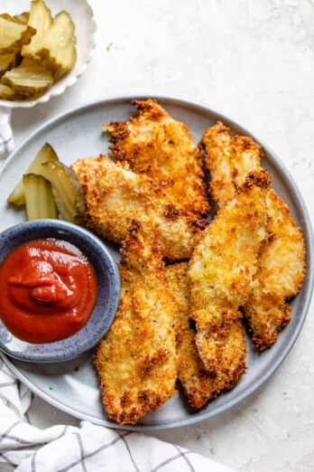Plate of pickle brined chicken tenders with ketchup and pickles on the side