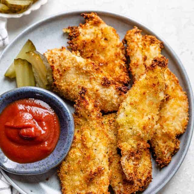Plate of pickle brined chicken tenders with ketchup and pickles on the side