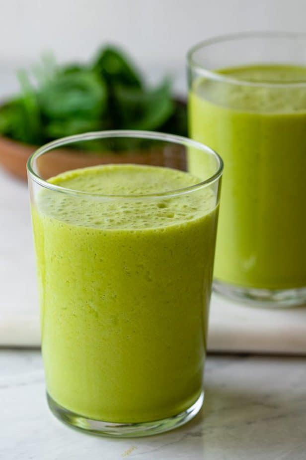 Close up of one cup of superfood smoothie with another one in the background along with baby spinach