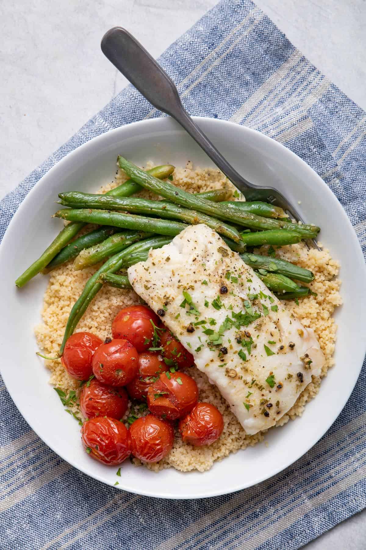 Sheet pan cod with green beans and tomatoes served over couscous