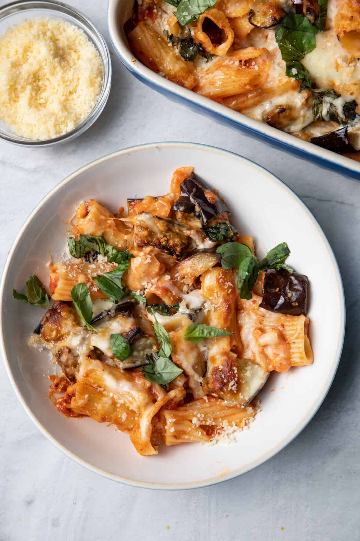 Eggplant pasta casserole served in a small bowl with parmesan cheese on the side