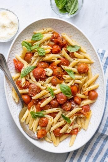 Long serving platter of roasted tomatoes tossed with penne pasta and garnished with basil.