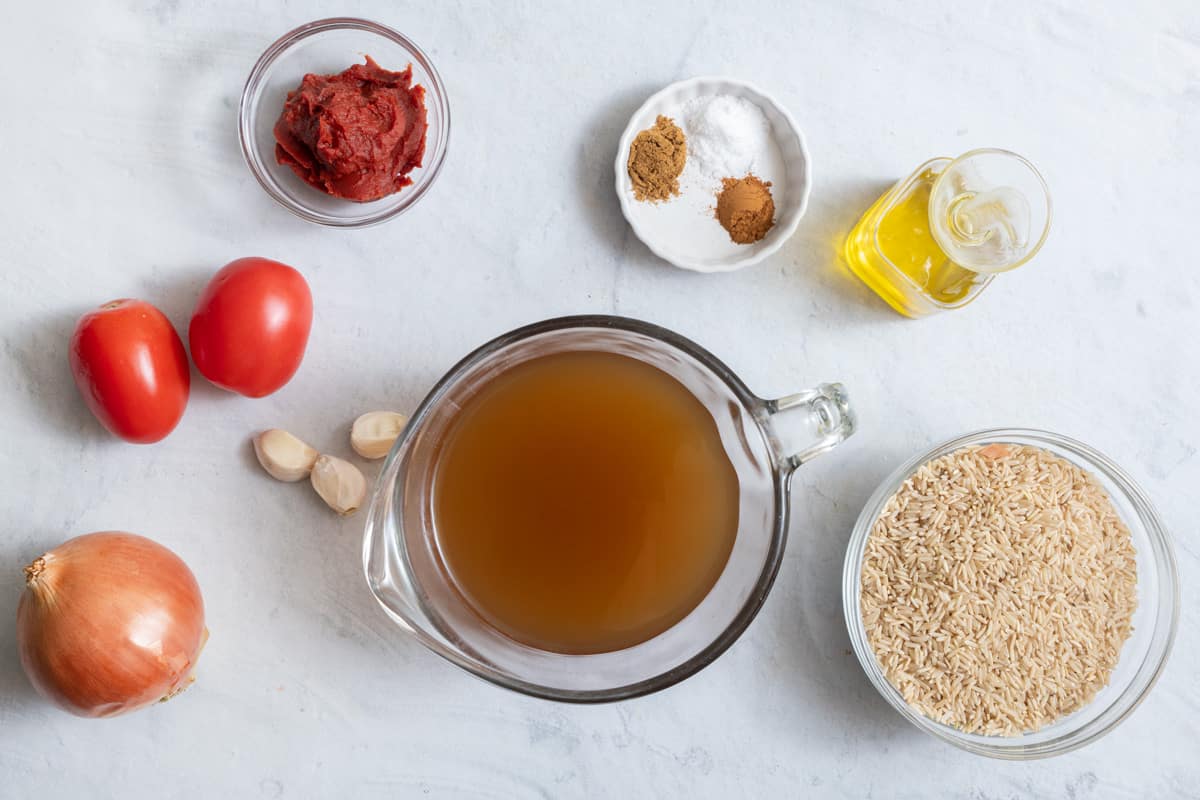 Ingredients to make the rice dish with tomatoes, tomato paste, onions, broth, spices and olive oil