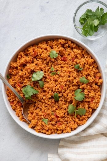 Large bowl of tomato rice with spoon inside and garnished with cilantrol