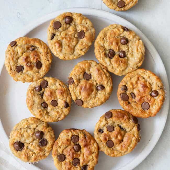 Overhead view of chocolate chip muffins on a large plate with one off to the side.