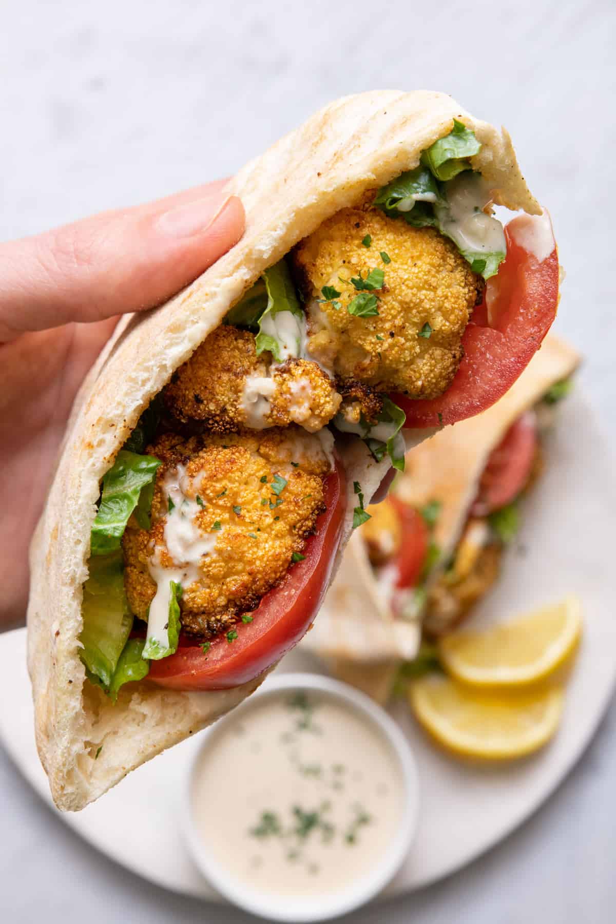 Close up shot of hand holding pita stuffed with cauliflower roasted in the oven with tahini sauce.