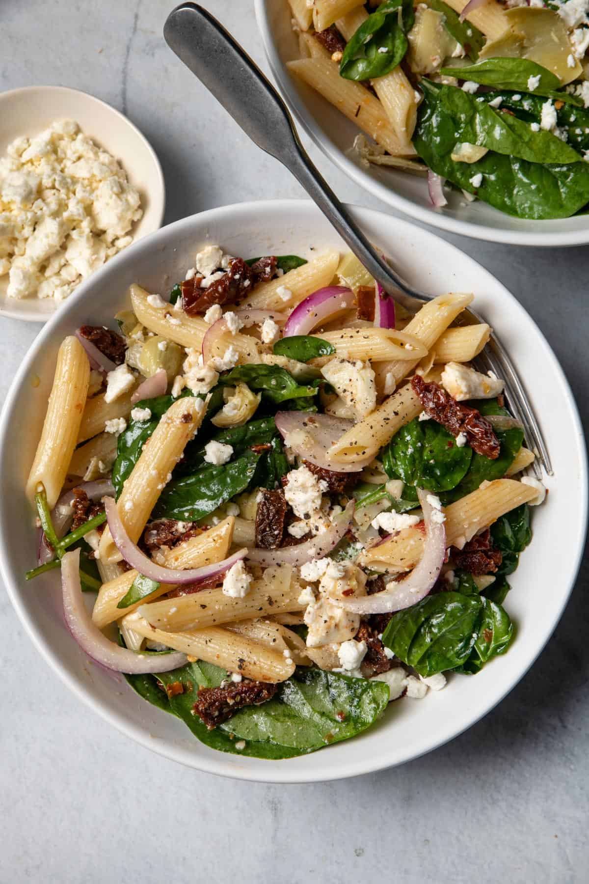 Spinach Pasta Salad in a white bowl on a table with another bowl next to it and feta cheese