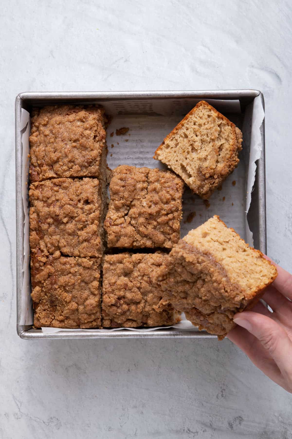 Pan with the cinnamon coffee cake and hand holding one of them to show the texture on the inside