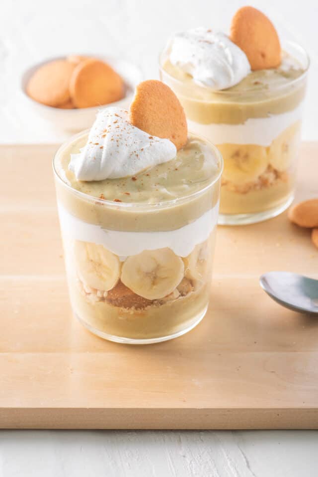 Two cups of banana pudding parfaits topped with whipped cream and a wafer.