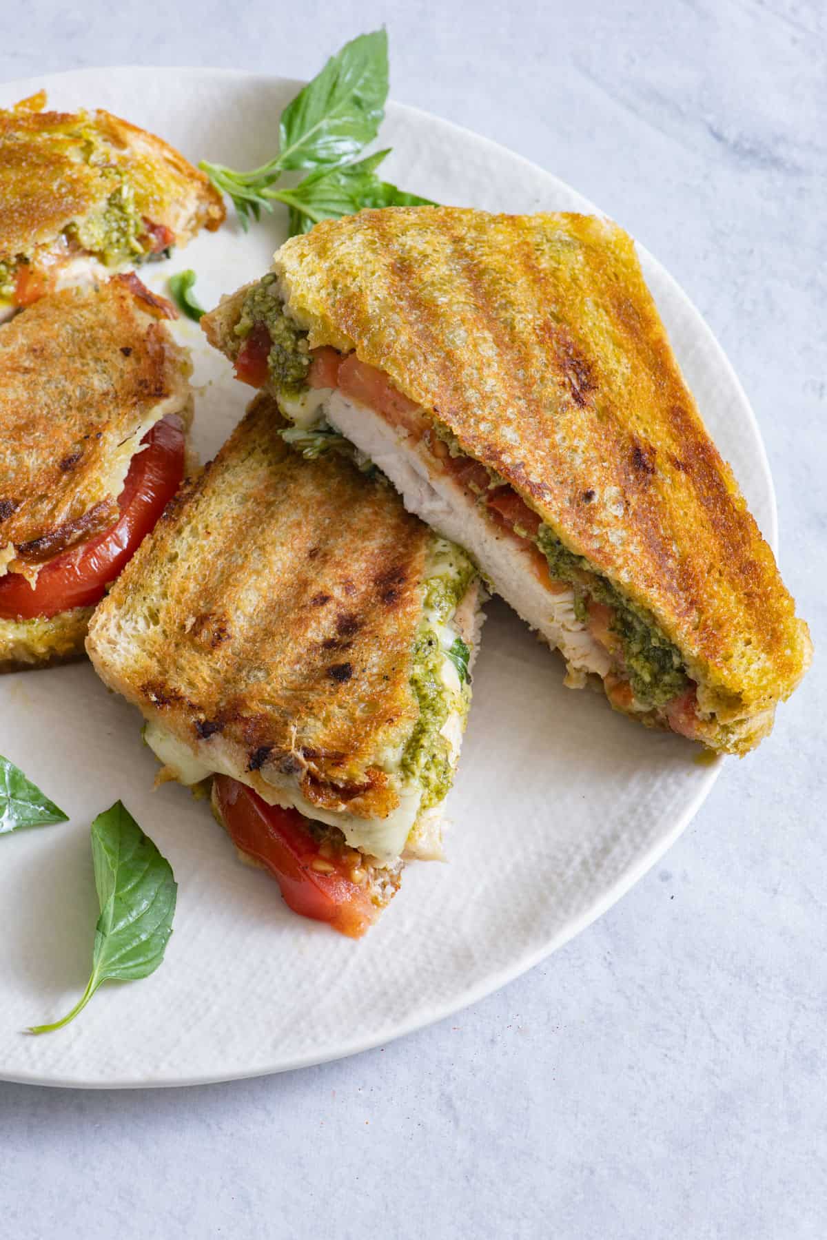 Panini sandwich sliced on a bias and stacked over each other, served on a large white plate with another sandwich.