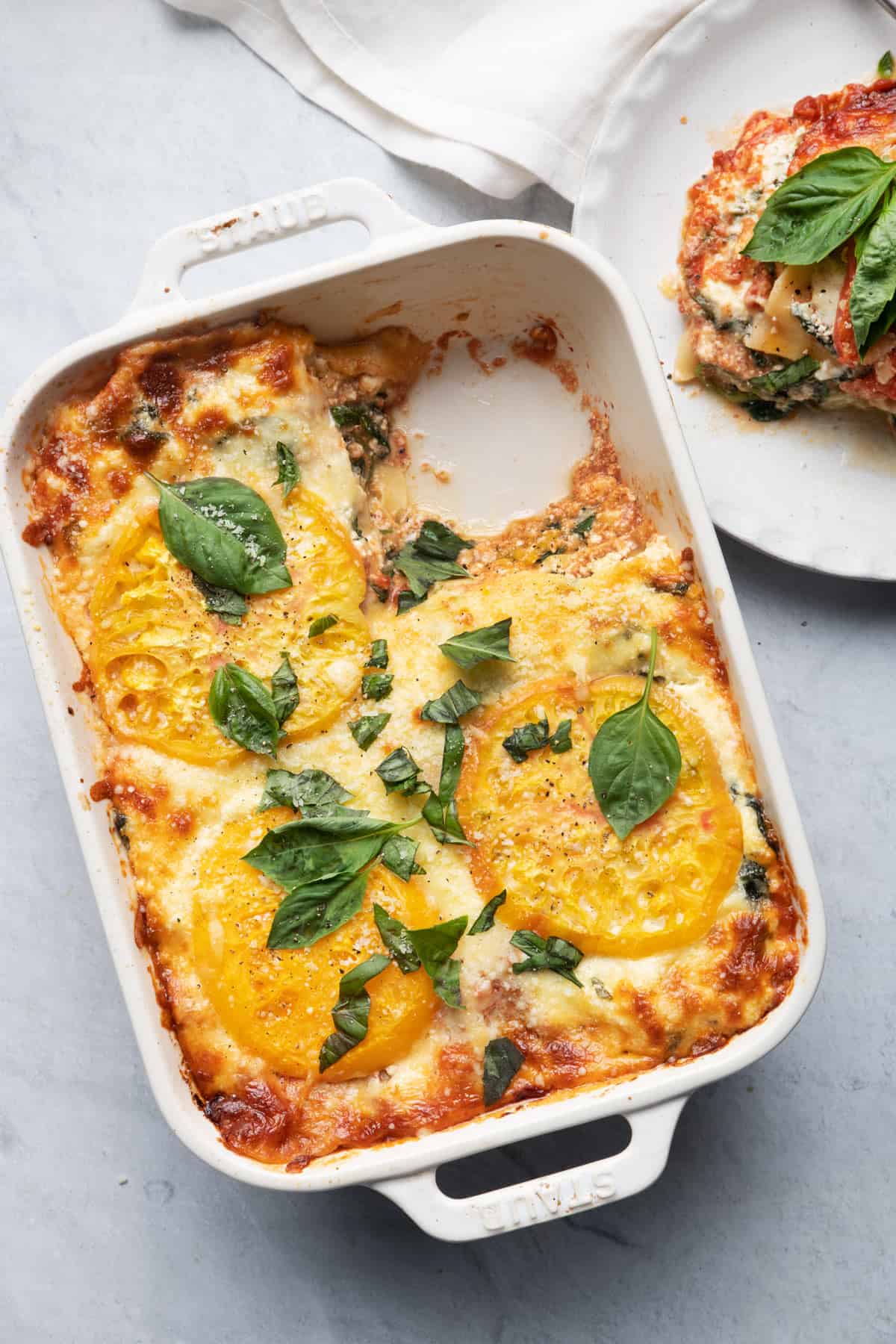 Tomato lasagna in baking dish with slice removed and served in plate nearby