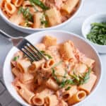 Fork taking bite of vegan creamy tomato pasta from bowl