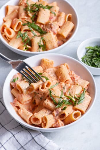 Fork taking bite of vegan creamy tomato pasta from bowl
