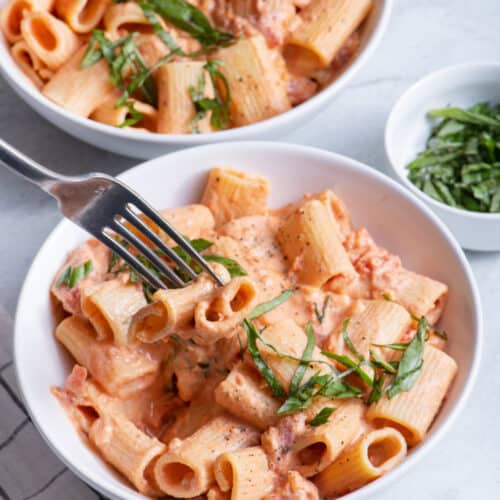 Fork taking bite of vegan creamy tomato pasta from bowl