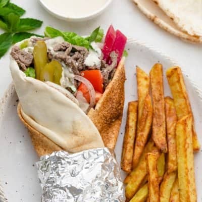 Beef shawarma wrap rolled up in a pita bread, alongside french fries