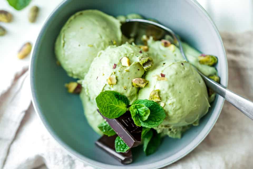 Three scoops of avocado ice cream in a bowl with garnish and a spoon. 