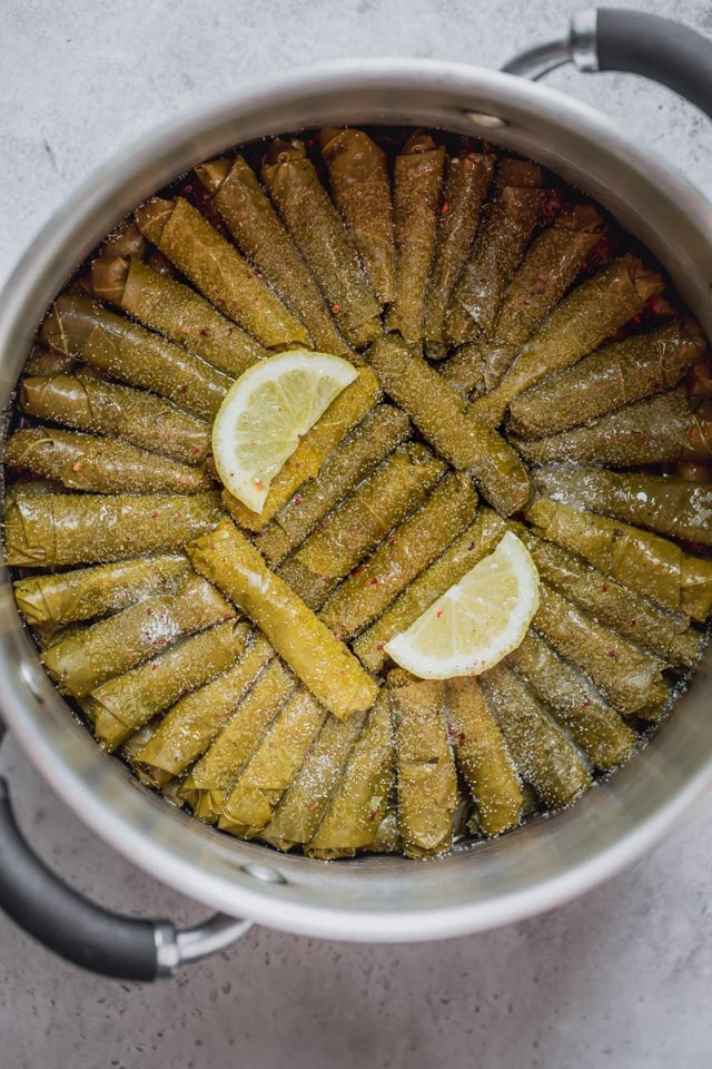 Vegetarian Stuffed Grape Leaves rolled up and stacked in a deep pot with seasoning on top and two slices of lemons - ready to be cooked.