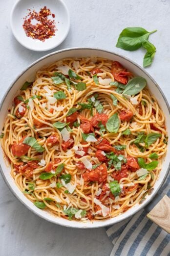 Pasta in skillet garnished with freshly shaved parmesan cheese and fresh basil.