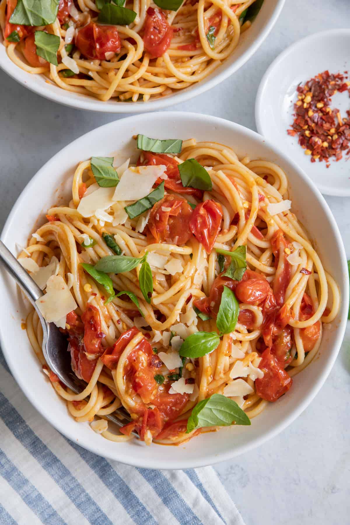 Two bowls of pasta in tomato sauce with fork in bowl and garnished with parmesan and fresh basil.