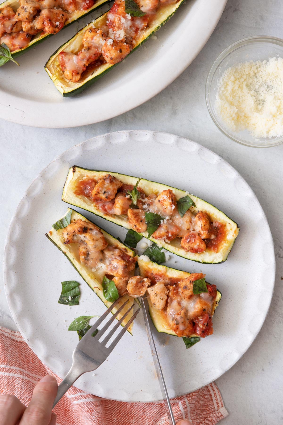 Close up cutting into zucchini boat on a small white plate with another plate off to the side.