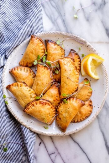 Final plated dish of the broccoli and cheese hand pies on a white plate with garnish and lemon slices