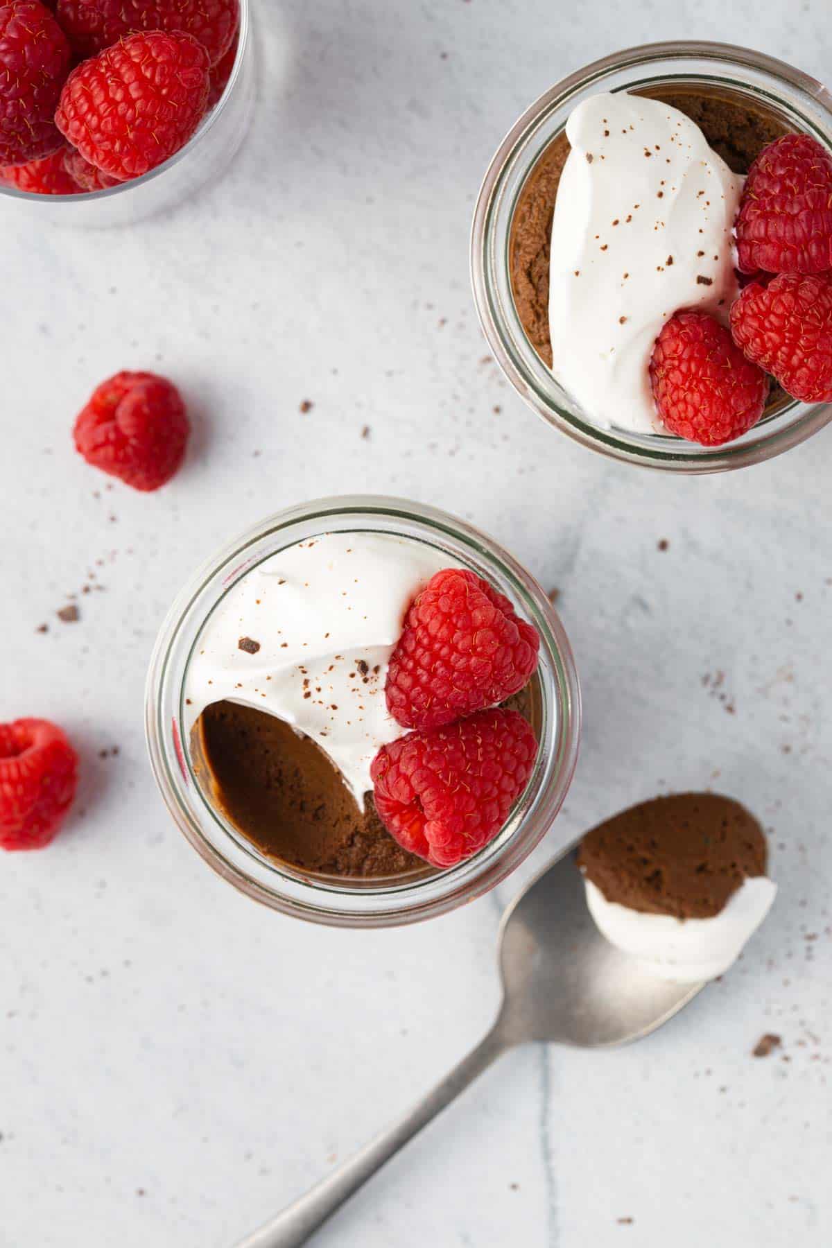 Top view of avocado chocolate mousse with bite taken out to show texture topped with fresh raspberries.