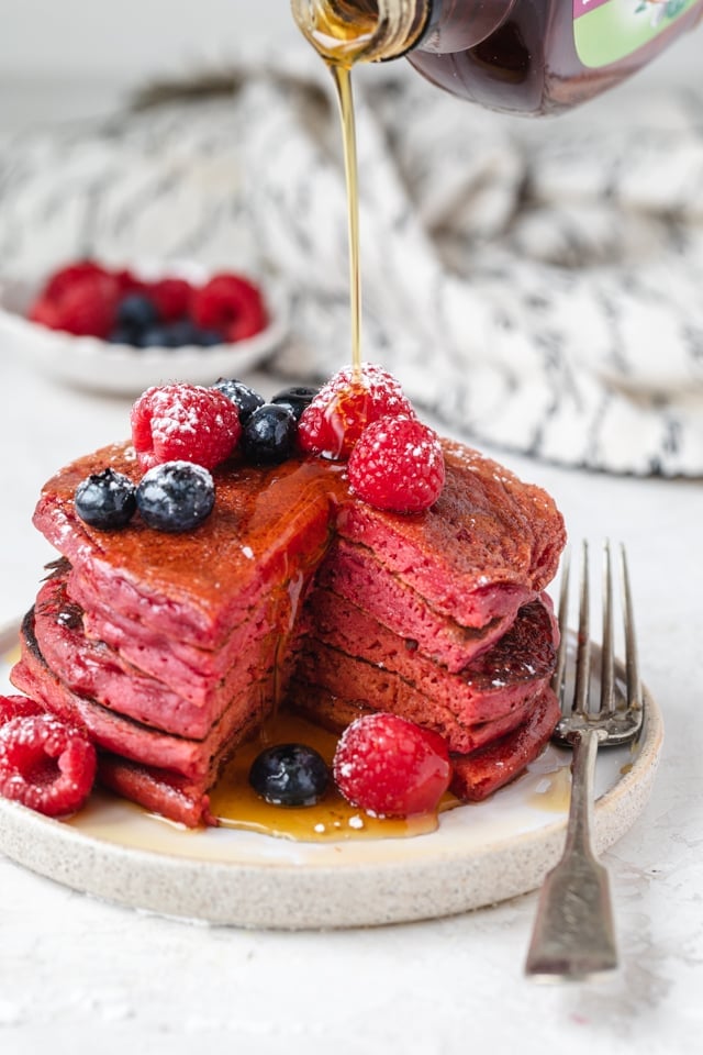 Stack of pink pancakes cut with maple syrup getting poured