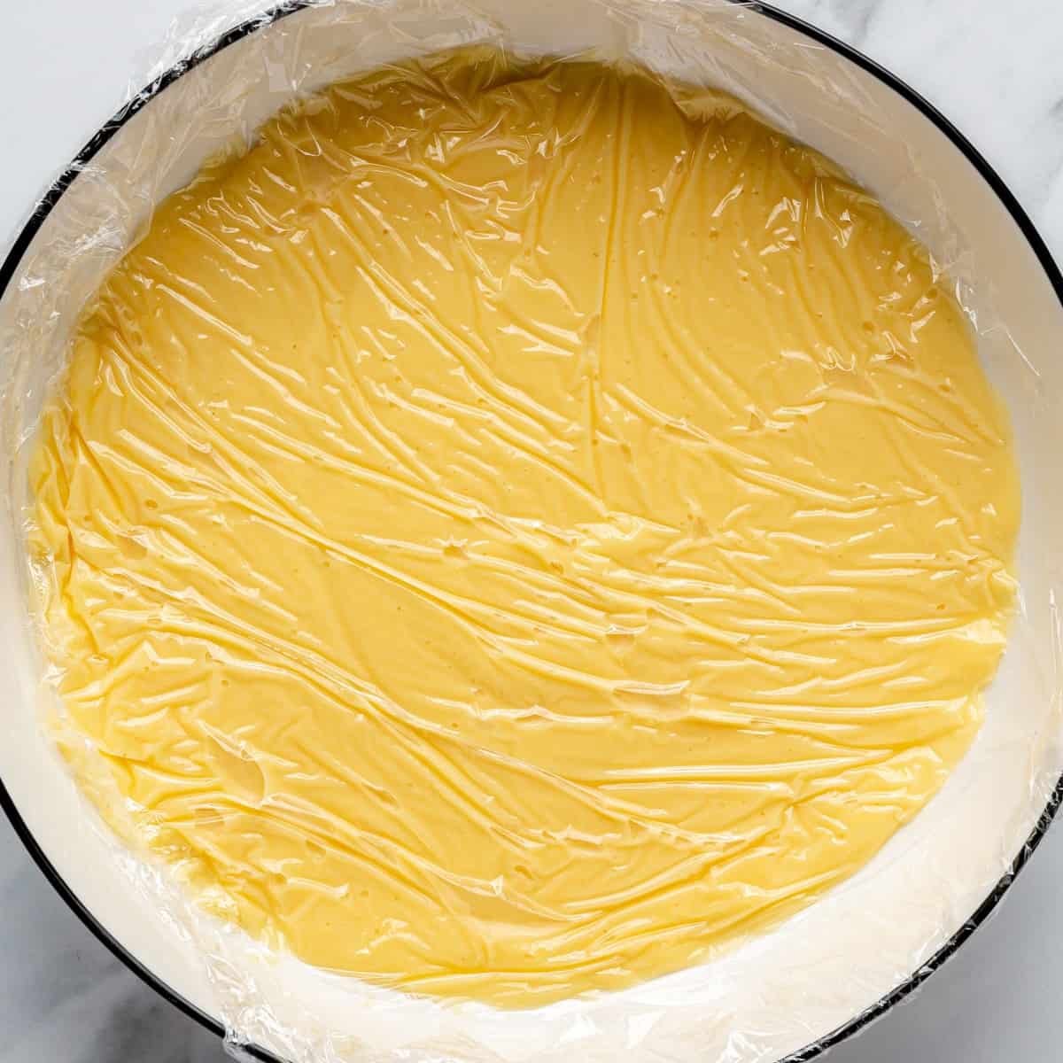 Pudding after straining in a bowl with plastic wrap pressed onto surface before refrigerating.