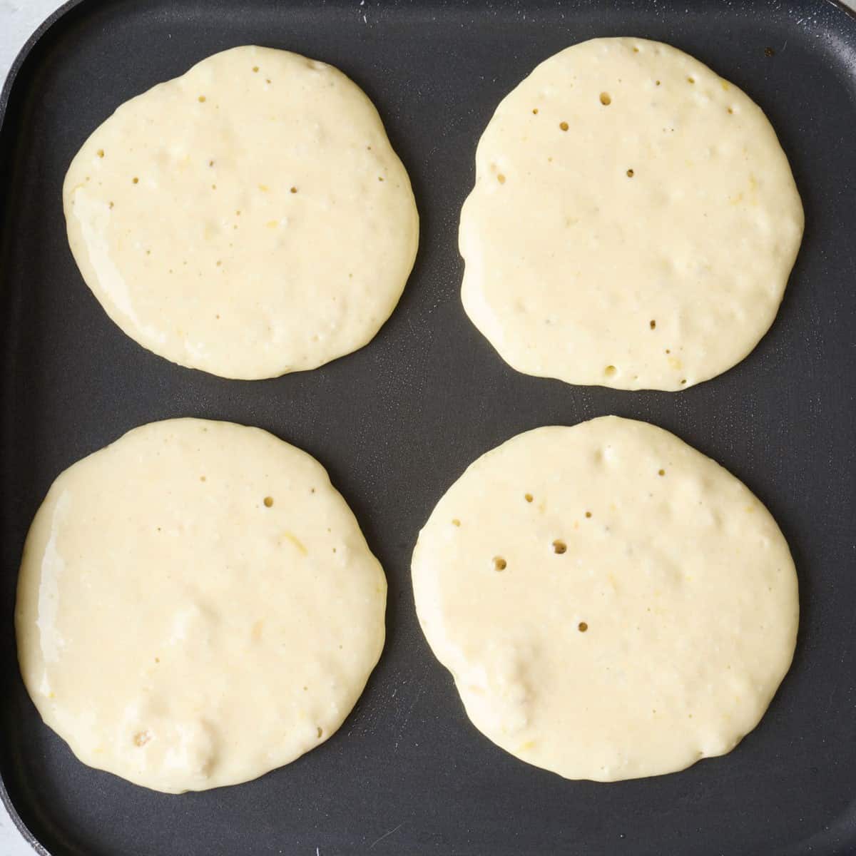 4 pancakes on a griddle before flipping.