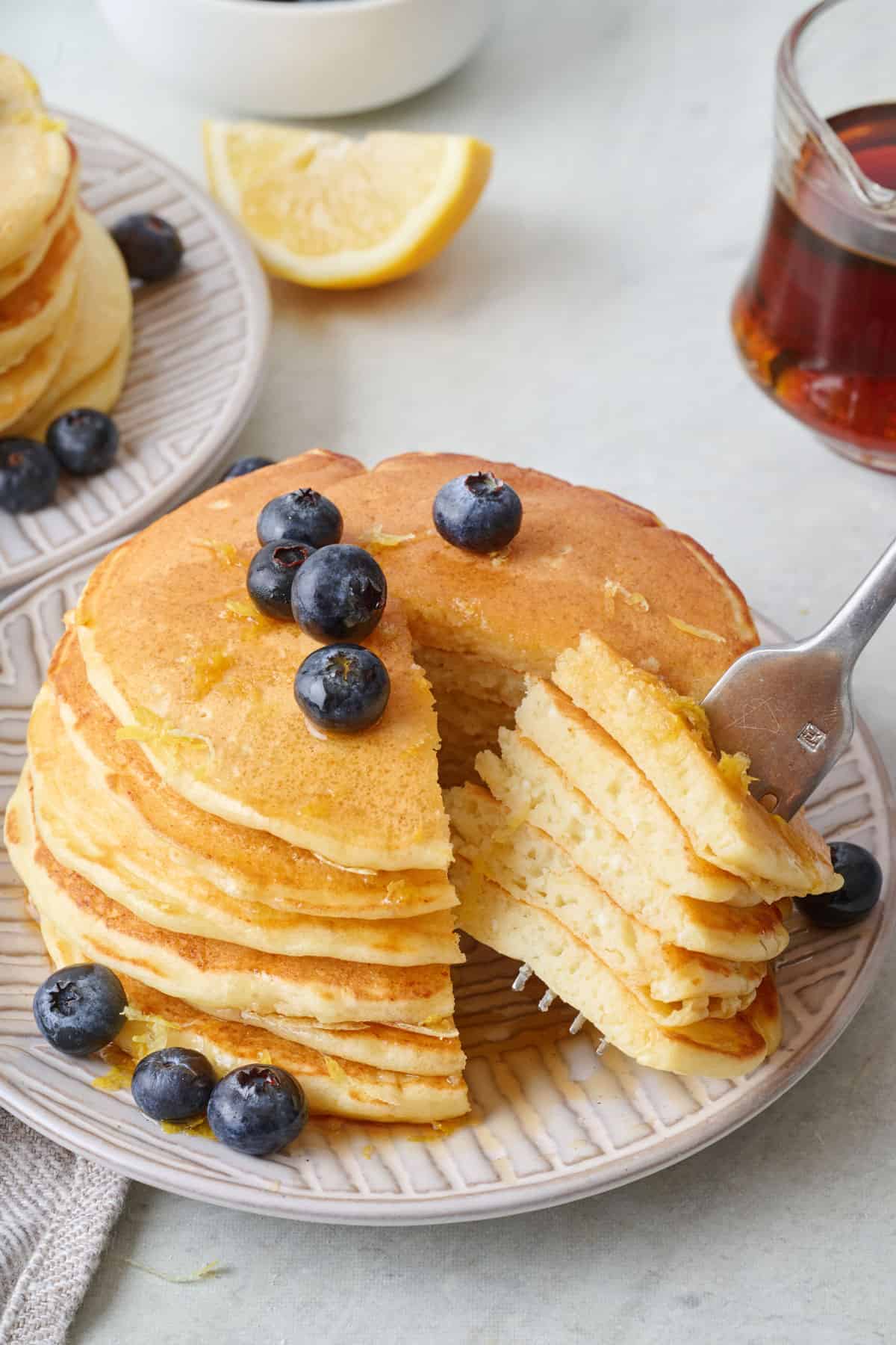 Fork pulling a bite away form a stack of lemon ricotta pancakes.