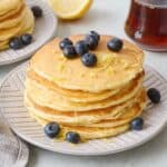 Stack of lemon ricotta pancakes with lemon zest and fresh blueberries on top.