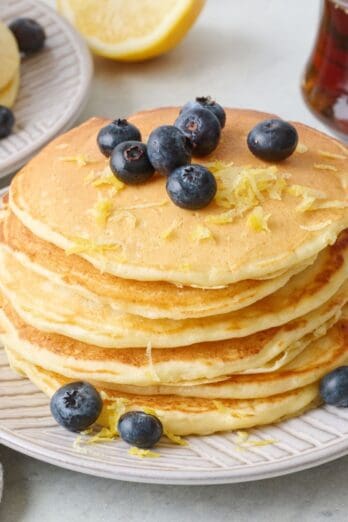 Stack of lemon ricotta pancakes with lemon zest and fresh blueberries on top.