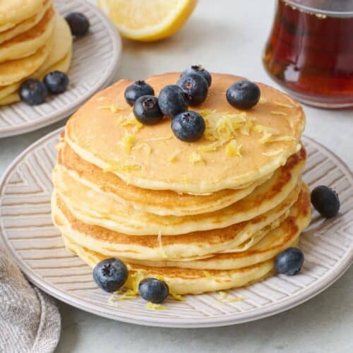 Stack of lemon ricotta pancakes with lemon zest and fresh blueberries on top.