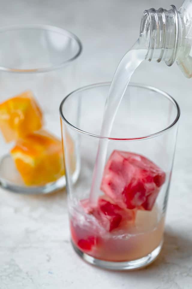 Pouring limeade into a glass with fruit cubes