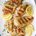 Grilled chicken breasts on a platter garnished with parsley and lemon wedges.
