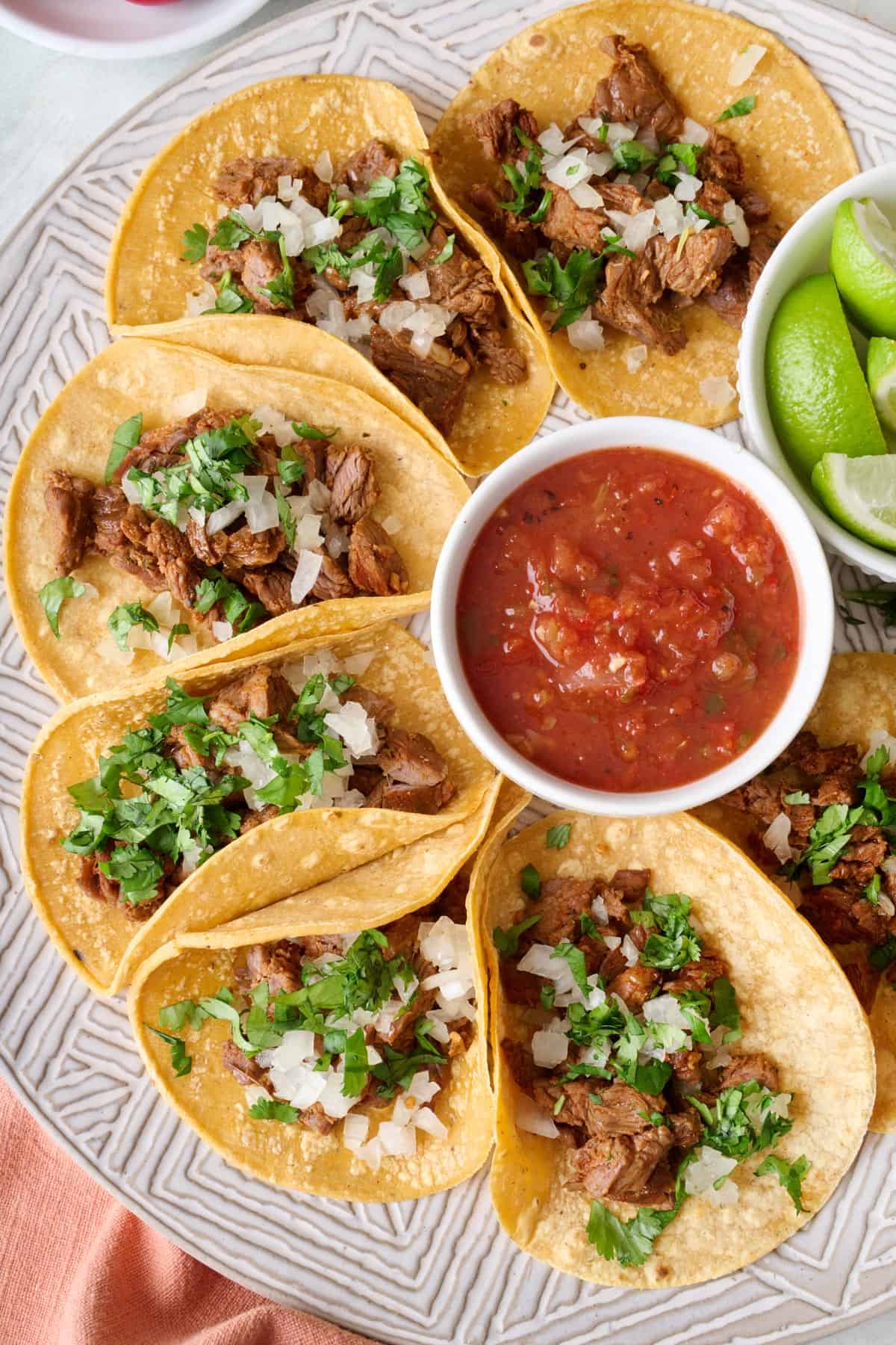 Homemade Mexican Street Tacos on a round platter with a small dish of salsa, garnished with fresh chopped cilantro and onions.
