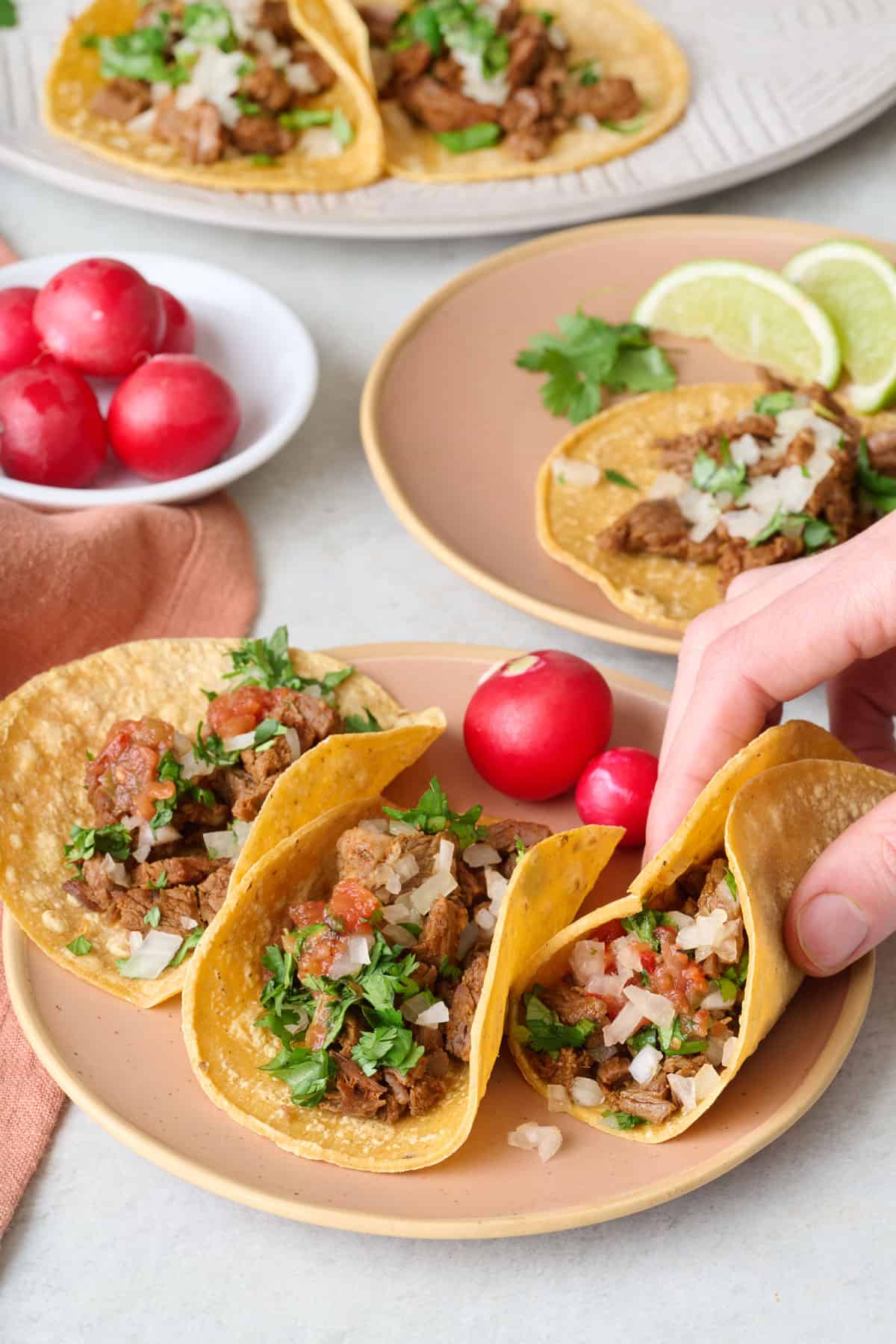 Mexican street tacos on a plate with a hand picking on up.