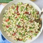 Couscous salad in a wide shallow bowl garnished with extra feta, serving spoon dipped inside with small jar of extra dressing nearby.