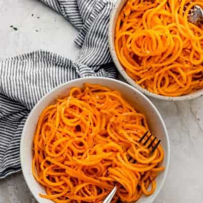 Two bowls of butternut squash noodles with forks inside bowls