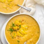 Two bowls of vegan corn chowder with spoons inside