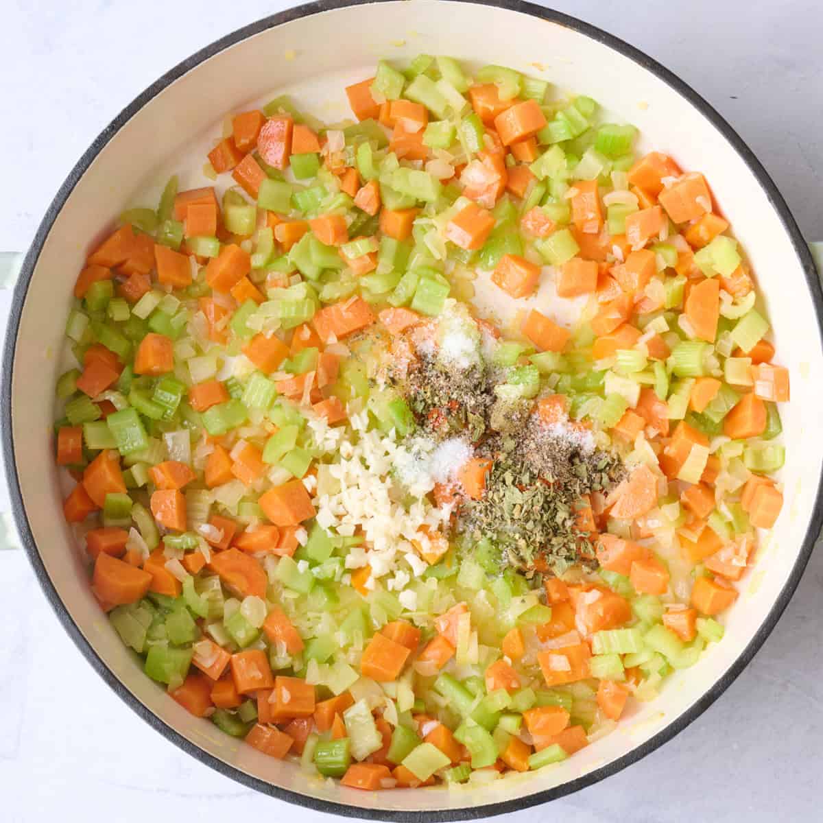 Onions, celery and carrots in a pot after sauteed with seasonings added on top.