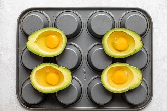 Cracked eggs inside 4 avocado halves before baking