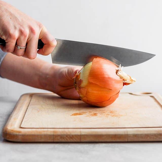 Large chef's knife cutting into onion on cutting board