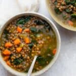 Two bowls of lentil kale soup with a spoon inside one bowl