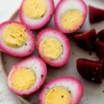 A plate of beet pickled eggs cut in half, with beets nearby.