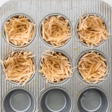 Potatoes added to a muffin tin.