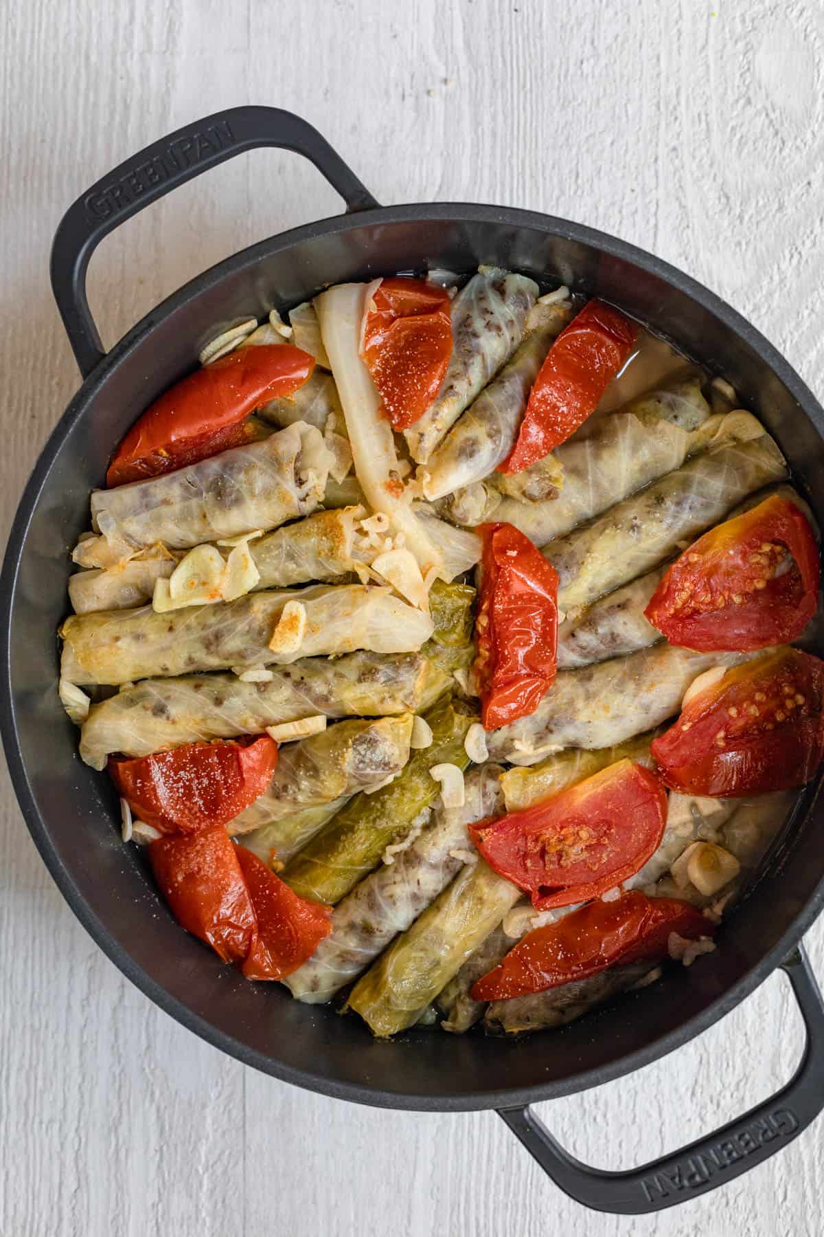 Showing the alternating layers of stuffed cabbage in a large pot with garlic, tomato slices and green peppers