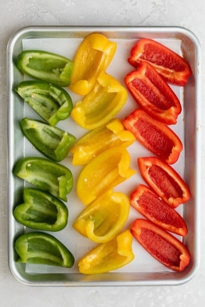 Bell peppers lined up on a baking dish.