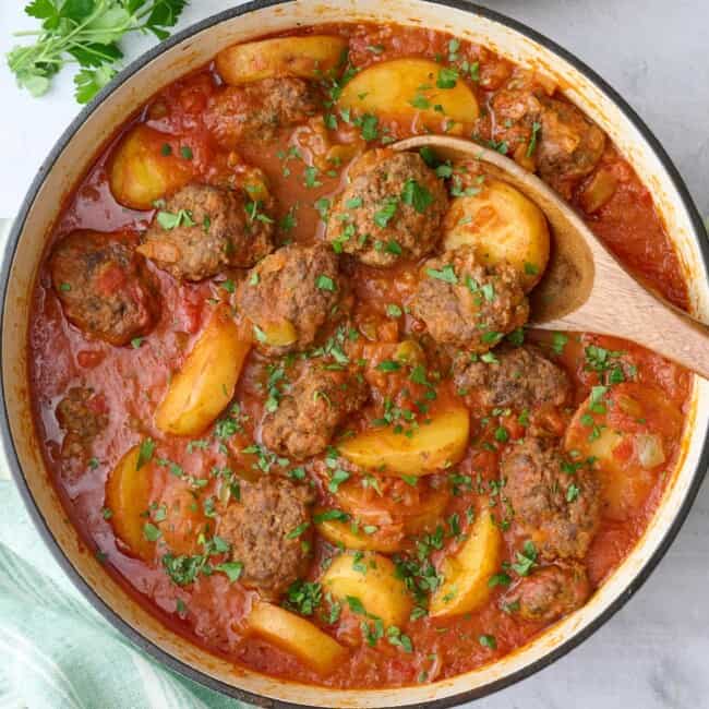 Kafta Potato Stew in the pot garnished lightly with chopped parsley, serving spoon, small dish of chopped parsley, and serving dish of Lebanese rice nearby.